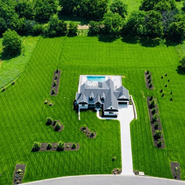 Aerial view of a modern white house with a pool and manicured diamond-patterned lawn.